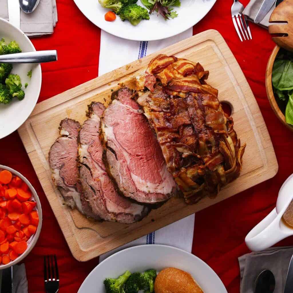 Prime rib wrapped in bacon on a cutting board