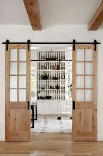 White farmhouse living room showcasing sliding barn doors with rustic wood finishes, adding character and functionality to the space, enhancing the room's modern farmhouse aesthetic.