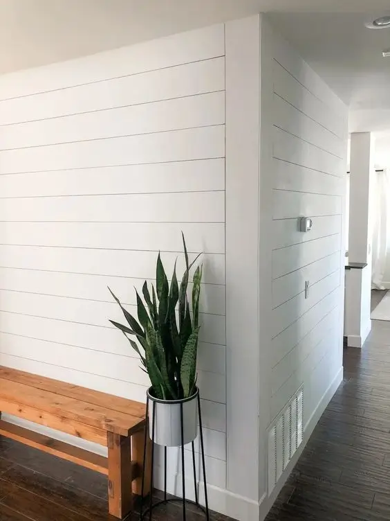 White shiplap wall in a modern farmhouse living room, offering a clean, rustic backdrop paired with natural wood furniture and neutral decor, enhancing the room's cozy, farmhouse aesthetic.