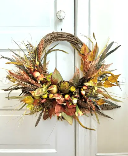 Grapevine wreath adorned with ornamental grasses, faux fruits, and pinecones, creating a rustic and natural fall decor piece perfect for your front door or home.