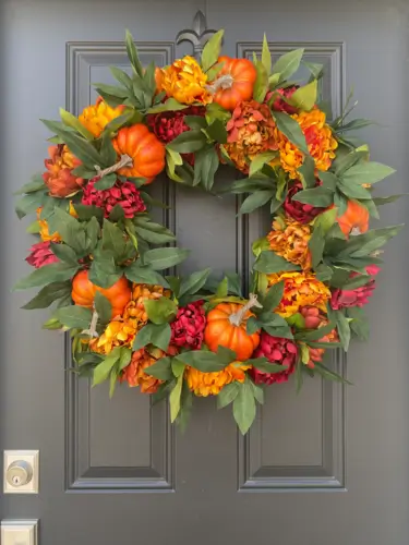 Pumpkin patch wreath with vibrant faux pumpkins and soft pink peonies, perfect for fall decor. Elegant autumn wreath for front door or seasonal home decoration.