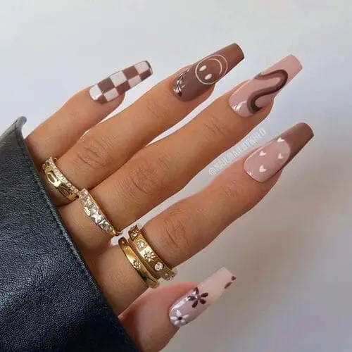 Brown and white mix and match nails with designs like checkered patterns, smiley faces, retro swirls, hearts with French tips, and floral accents—a creative, trendy manicure idea.