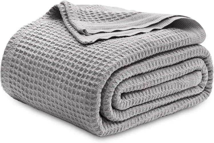 Grey woven blanket adding cozy texture to a serene light grey and white bedroom. Perfect for bedroom inspiration, available for readers to buy on Amazon.