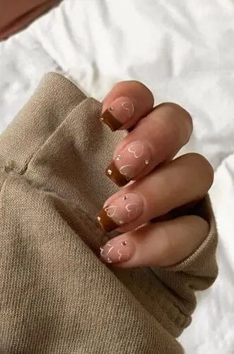 Elegant brown French manicure with delicate white hearts and crystal accents—stylish, romantic nail art perfect for a chic and whimsical look.