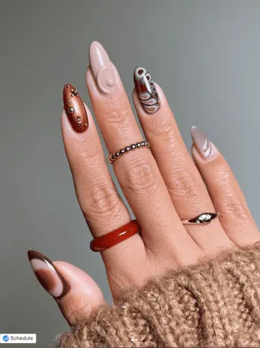 Incredible brown sculpted nails with unique designs: thumb features a brown and cream aura, index finger has a copper glitter base with 3D gold drops, middle nail shows a beige sculpted swirl, ring finger highlights a retro butterfly-inspired art, and pinkie nail has a velvet cat eye polish with a 3D swirl accent.