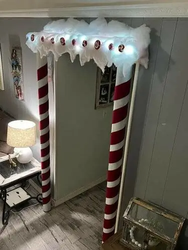 DIY candy cane pillars for doorway Christmas decoration, wrapped in red velvet ribbon with snow accents and fairy lights.