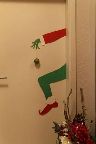 Christmas door decoration ideas: The Grinch holding a Christmas ornament for a playful holiday door design