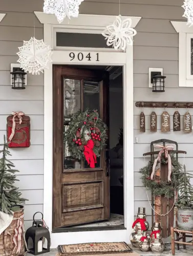 Vintage farmhouse Christmas door decorations with rustic wreaths, wooden rustic sleighm vintage maibox, custom name tags, paper snowflakes, and iron candle accents for a nostalgic holiday feel.