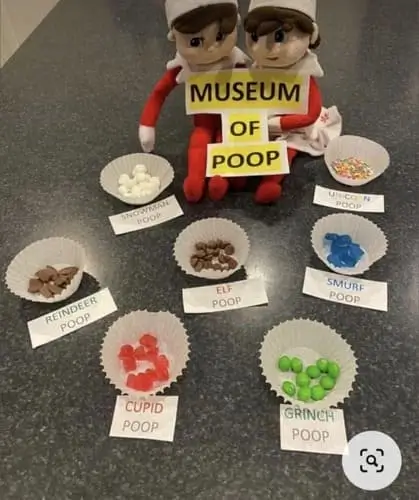 Elf on the Shelf next to a "Museum of Poop" sign with candies in muffin liners: red jujubes labeled as Cupid poop, chocolate chips as elf poop, mini marshmallows as snowman poop, green M&Ms as Grinch poop, blue gummies as Smurf poop, and sprinkles as unicorn poop. A funny and creative holiday idea for kids.