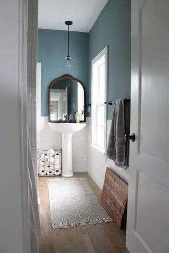 White pedestal sink in a narrow bathroom with light wood floor and minimalist decor for a spacious look.