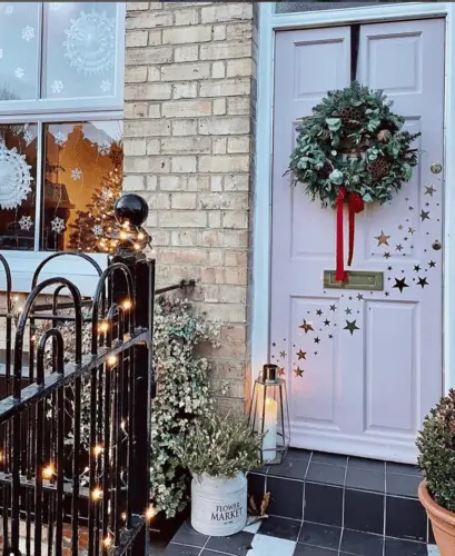 Christmas front door decorated with star decals, a festive wreath, a metal flower bucket filled with greenery, and a candle lantern, creating a warm, vintage-inspired holiday entrance.