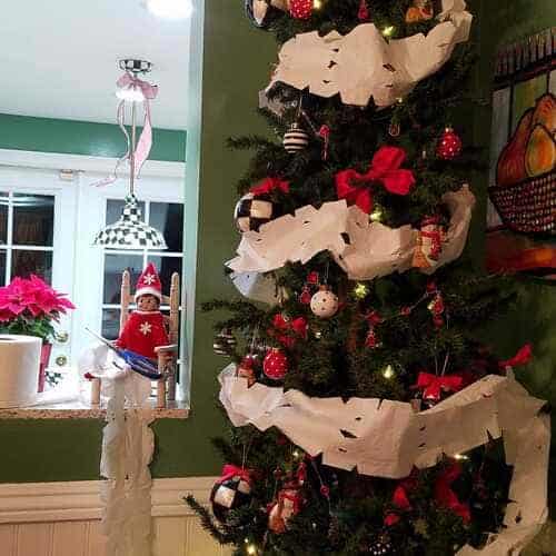 The best Elf on the Shelf ideas! Christmas tree wrapped in toilet paper snowflake garland made by Elf on the Shelf, with ornaments and festive holiday decorations.