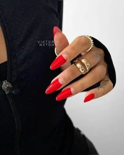 Long cherry red half-moon nails for Valentine’s Day, featuring a chic bare crescent at the cuticle, perfectly paired with gold jewelry for an elegant and bold look.