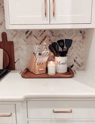 Chic and trendy apartment kitchen decor featuring a styled knife set, candle, and utensil holder on a sleek wooden block, paired with a modern backsplash and updated cabinet hardware for a fresh look.