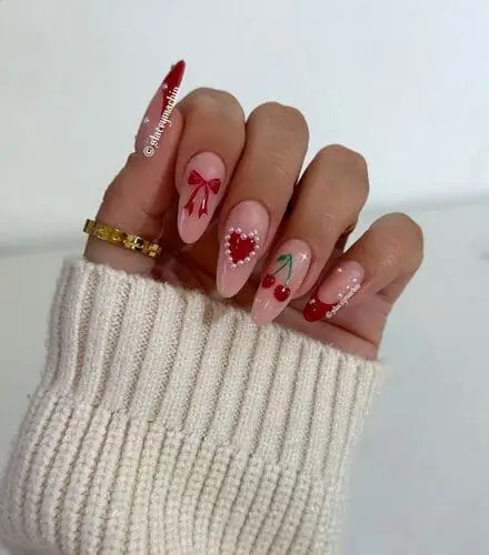 Valentine's Day nail art featuring alternating designs such as a coquette bow, a heart with white dots, cute cherries, and red French tips with pearl accents. A playful and stylish look perfect for the holiday.