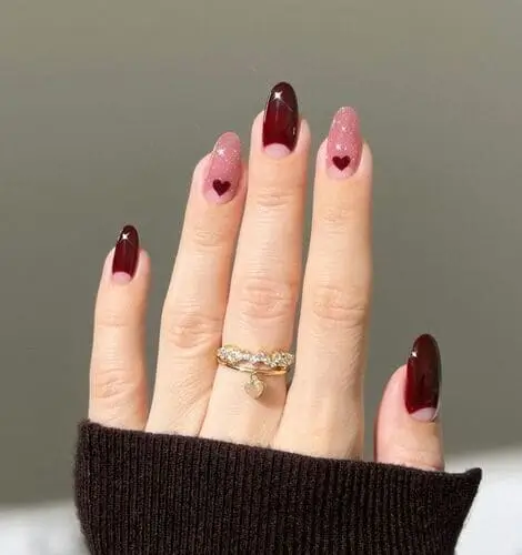 Valentine’s nails featuring merlot red half moons alternating with pink sparkly nails adorned with mini merlot red hearts for a chic and romantic design.