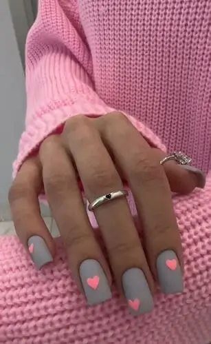 Matte grey Valentine’s nails with small neon pink hearts for a modern and playful twist on romantic nail designs.