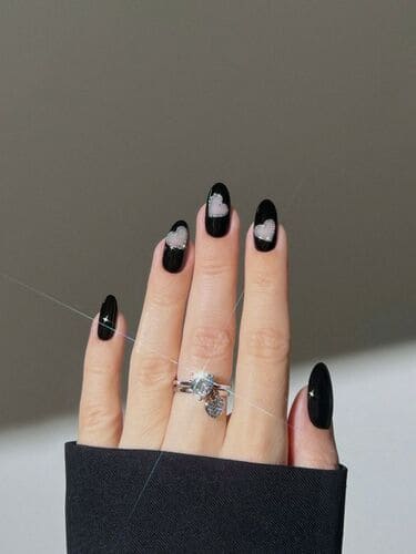 Bold black negative space Valentine’s nails with heart accents for a modern, minimalist, and edgy manicure.