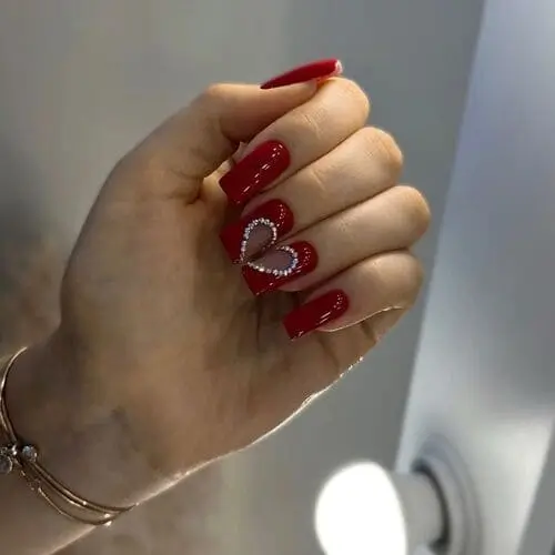 Square red Valentine’s nails with crystal accents on the middle and ring fingers that form a heart when joined, adding shimmer and opulence to the romantic design.